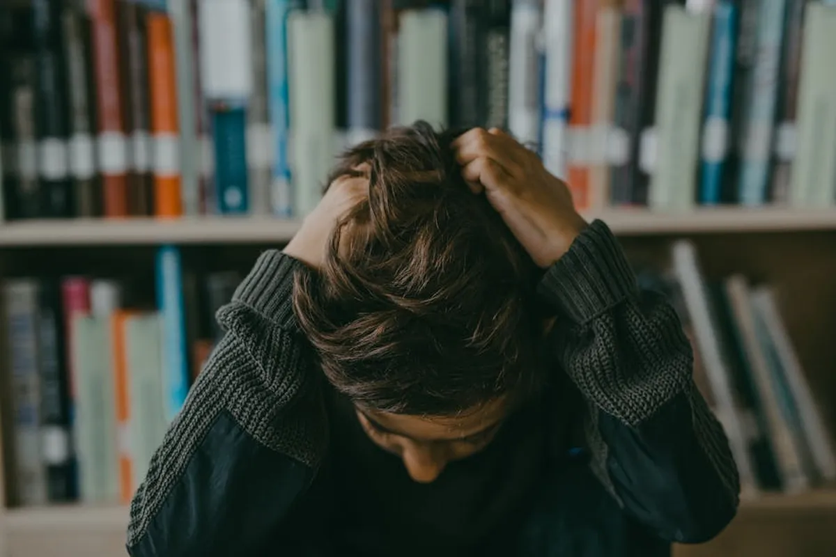 Pessoa estudando com expressão pensativa em frente a pilha de livros