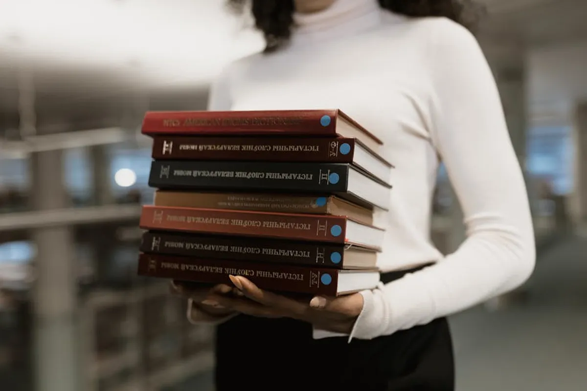 Pilha de livros e artigos científicos sobre mesa de pesquisadora em biblioteca