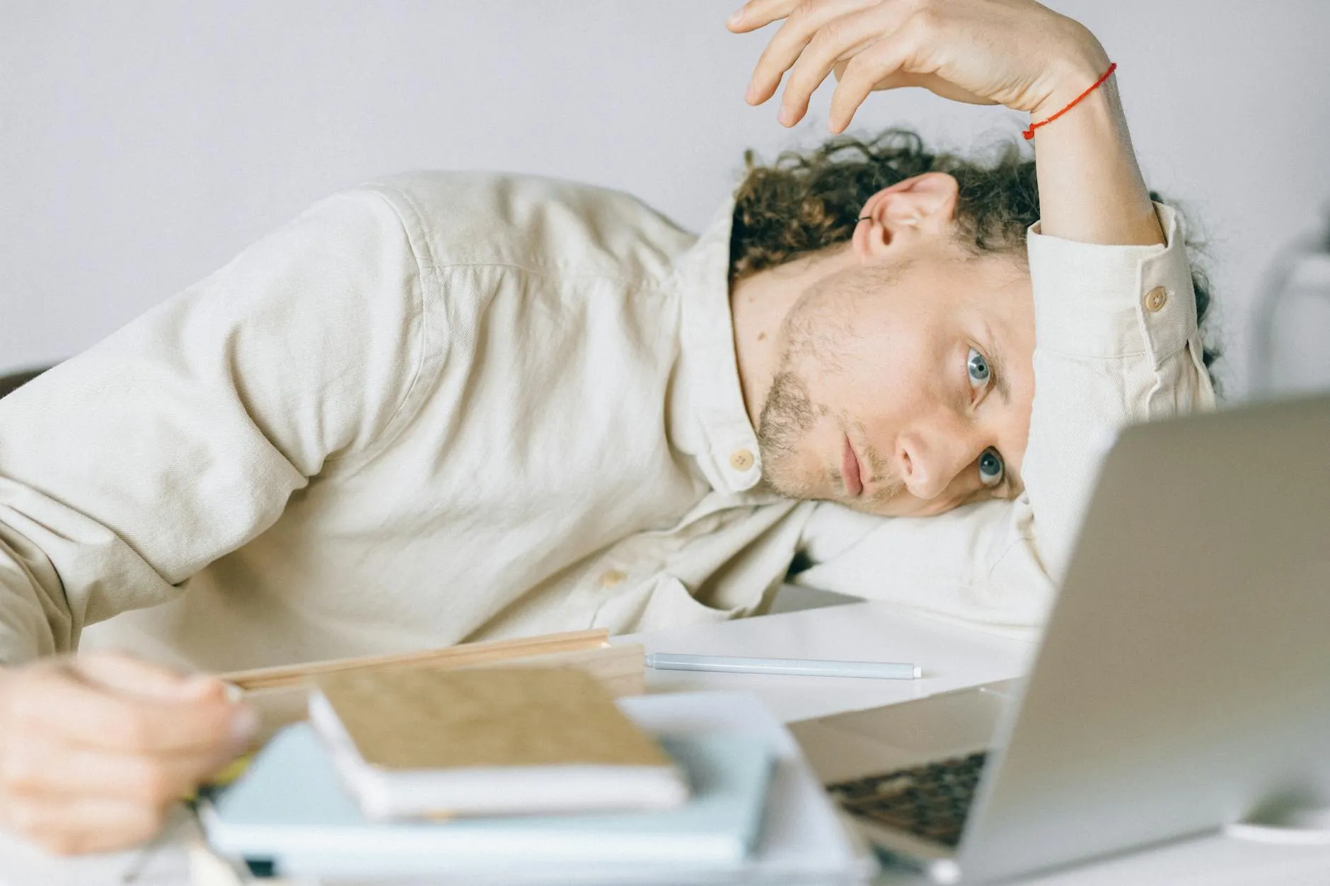 Pessoa exausta recostada em mesa de trabalho com cadernos e canetas ao redor