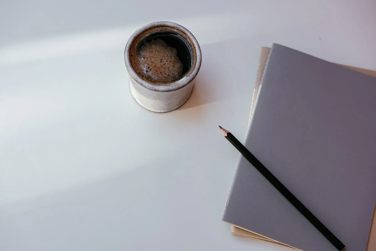 Xícara de café ao lado de livros acadêmicos e caderno de anotações em mesa de estudos