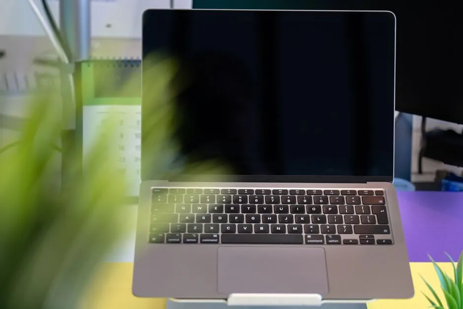 Pessoa trabalhando em um laptop com telas coloridas de design visual ao fundo, representando criação de apresentação acadêmica.