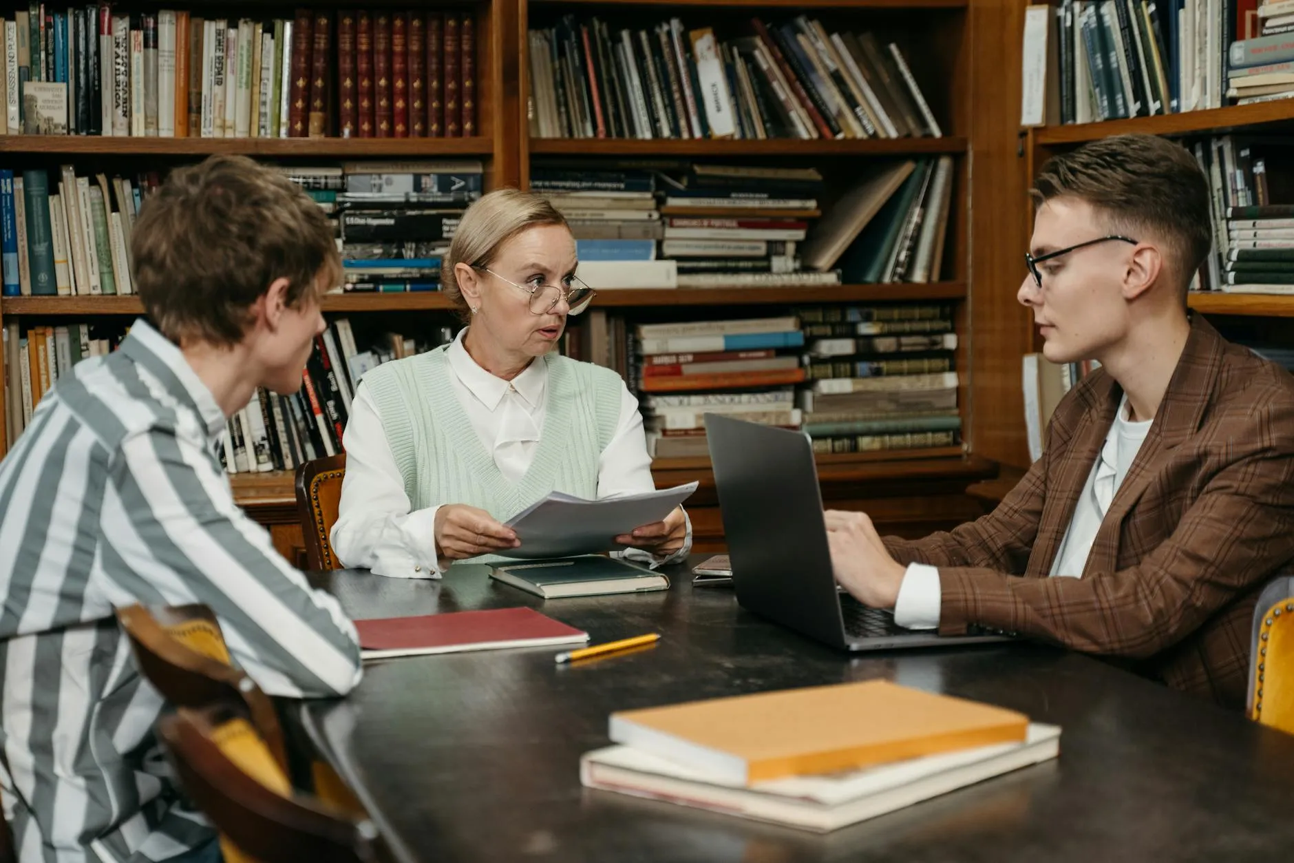 Dois professores e um estudante em discussão ao redor de uma mesa com papéis