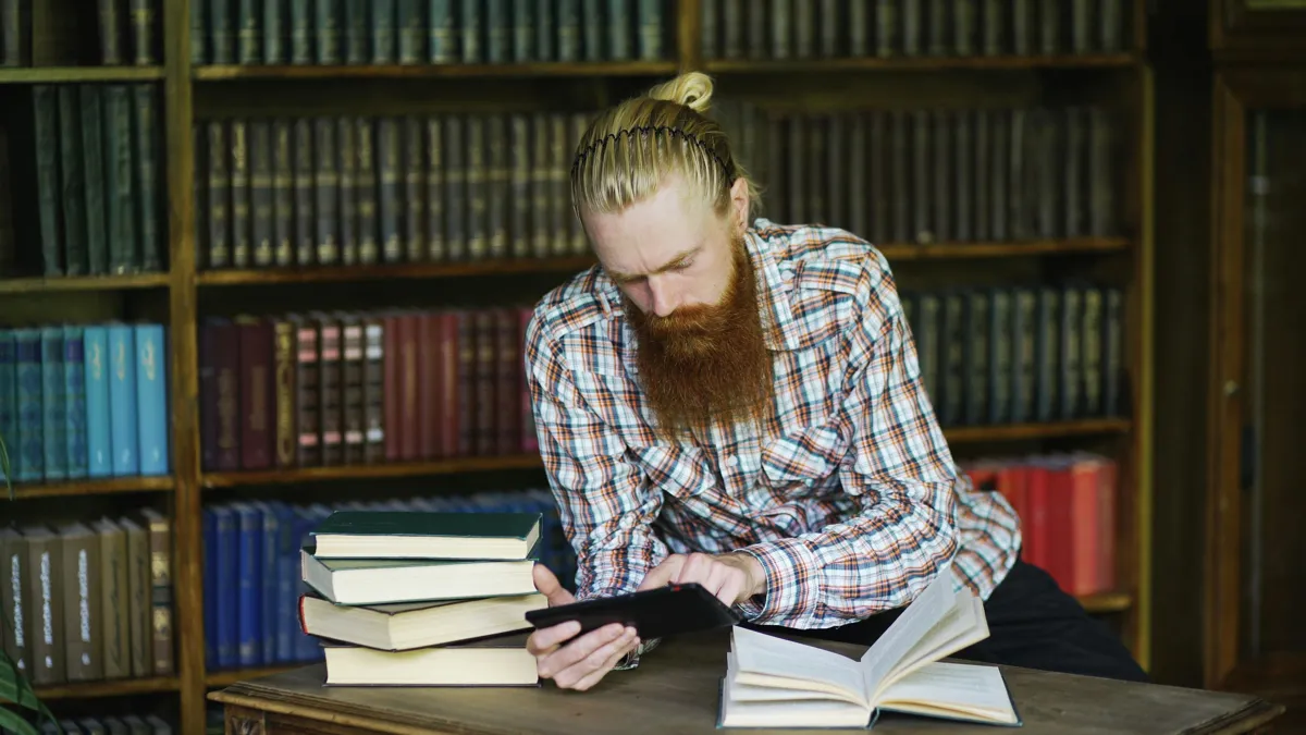 Pesquisadora lendo artigo científico em biblioteca universitária com outros livros ao fundo.
