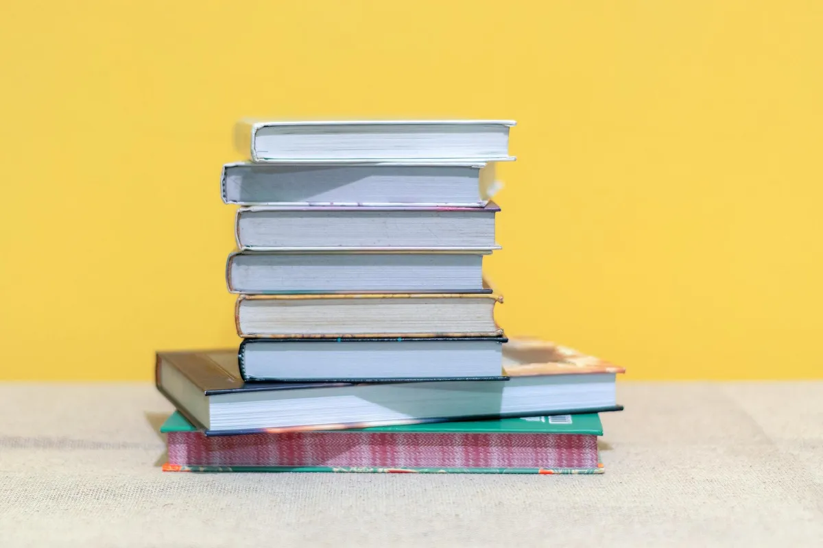 Pilha de livros acadêmicos sobre mesa com caderno de anotações aberto