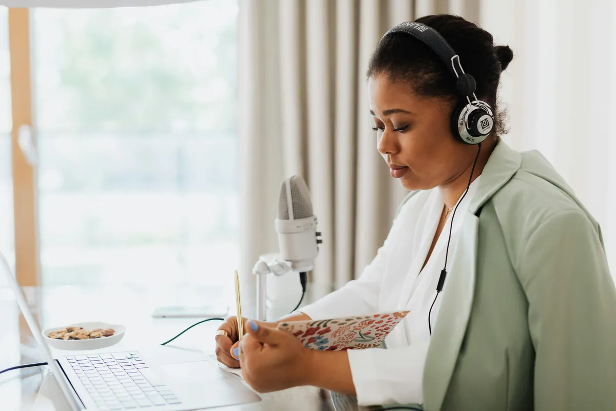 Pesquisadora ouvindo podcast com fones enquanto anota referências em caderno