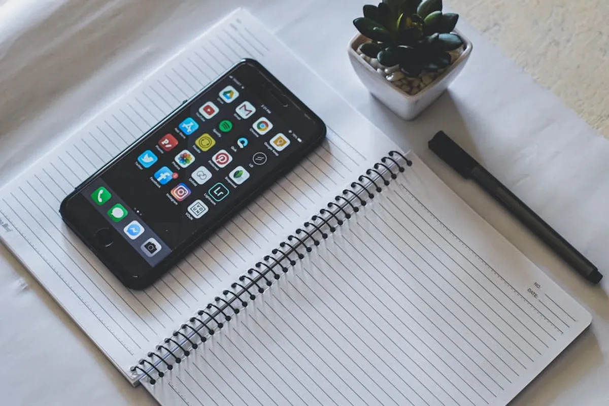 Smartphone com redes sociais ao lado de caderno de anotações acadêmicas