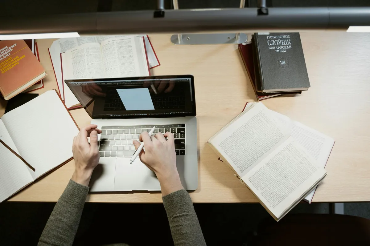 Pessoa digitando referências em um notebook com anotações ao lado