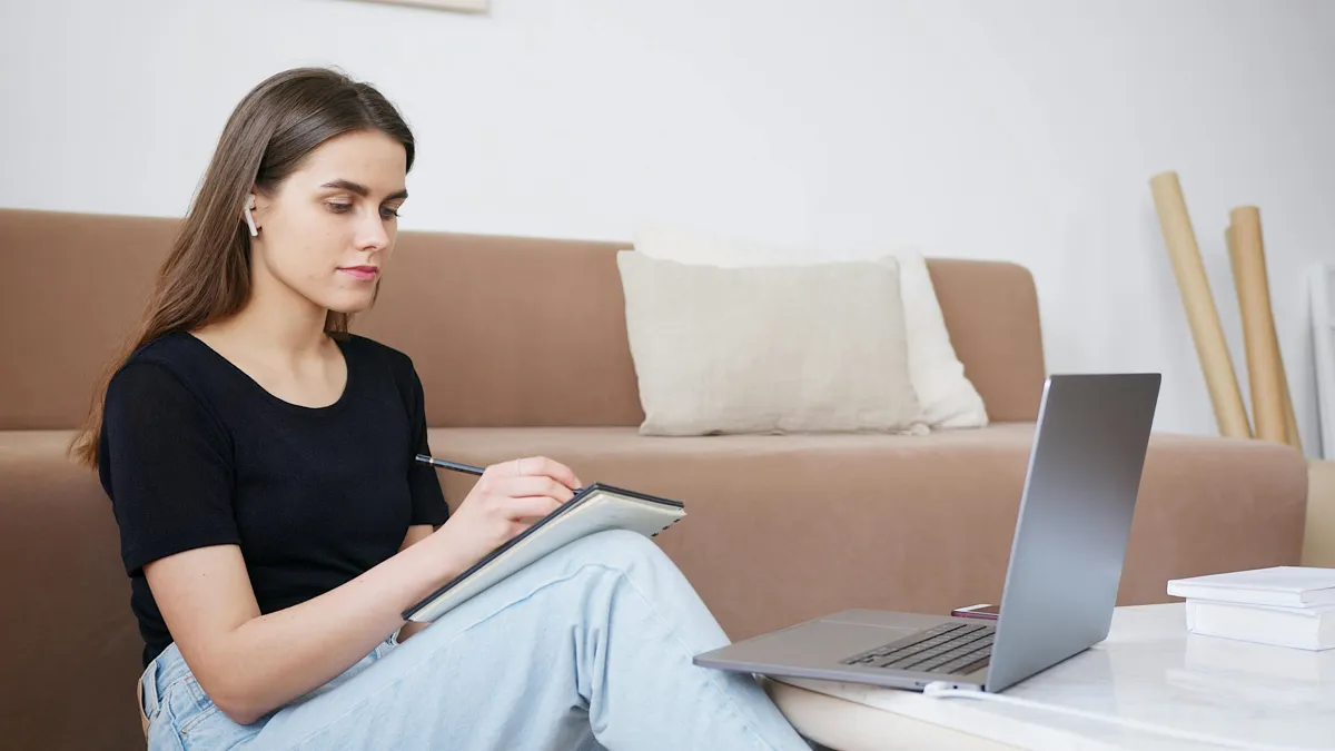 Estudante assistindo video no computador com caderno de anotacoes ao lado para pesquisa academica