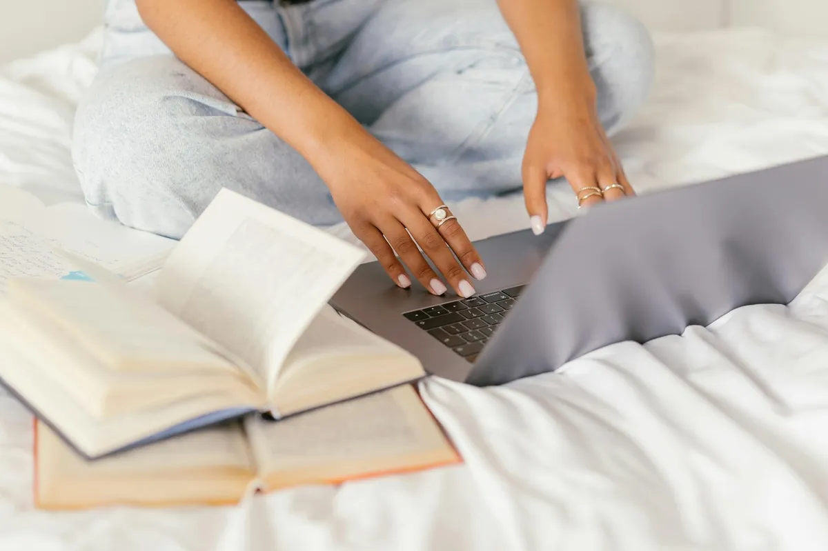 Pessoa trabalhando no computador com livros acadêmicos ao lado