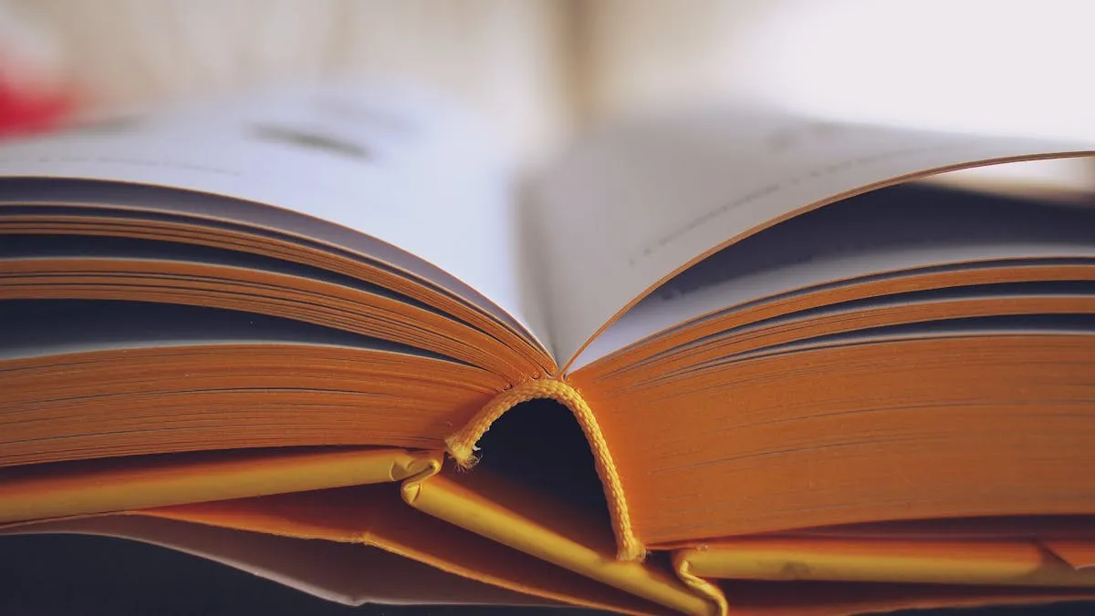Mãos segurando livro acadêmico aberto em biblioteca universitária