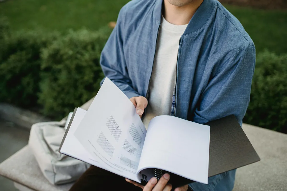 Estudante pensativo diante de livros e anotações, planejando pesquisa acadêmica