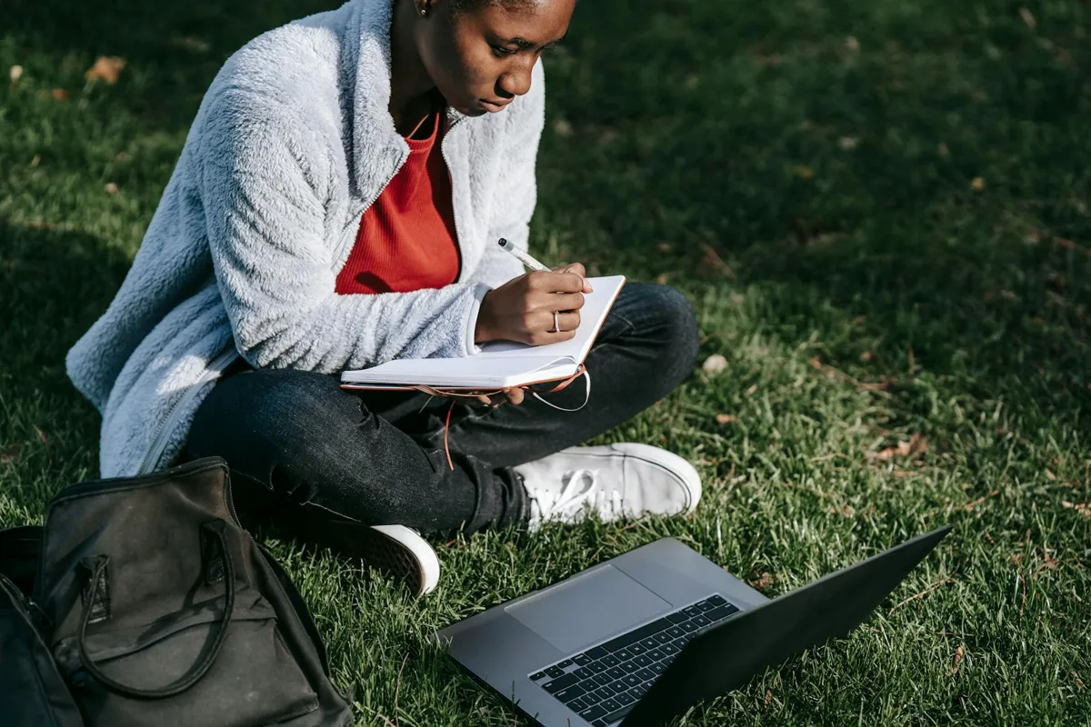 Estudante escrevendo TCC no computador com caderno de anotações ao lado