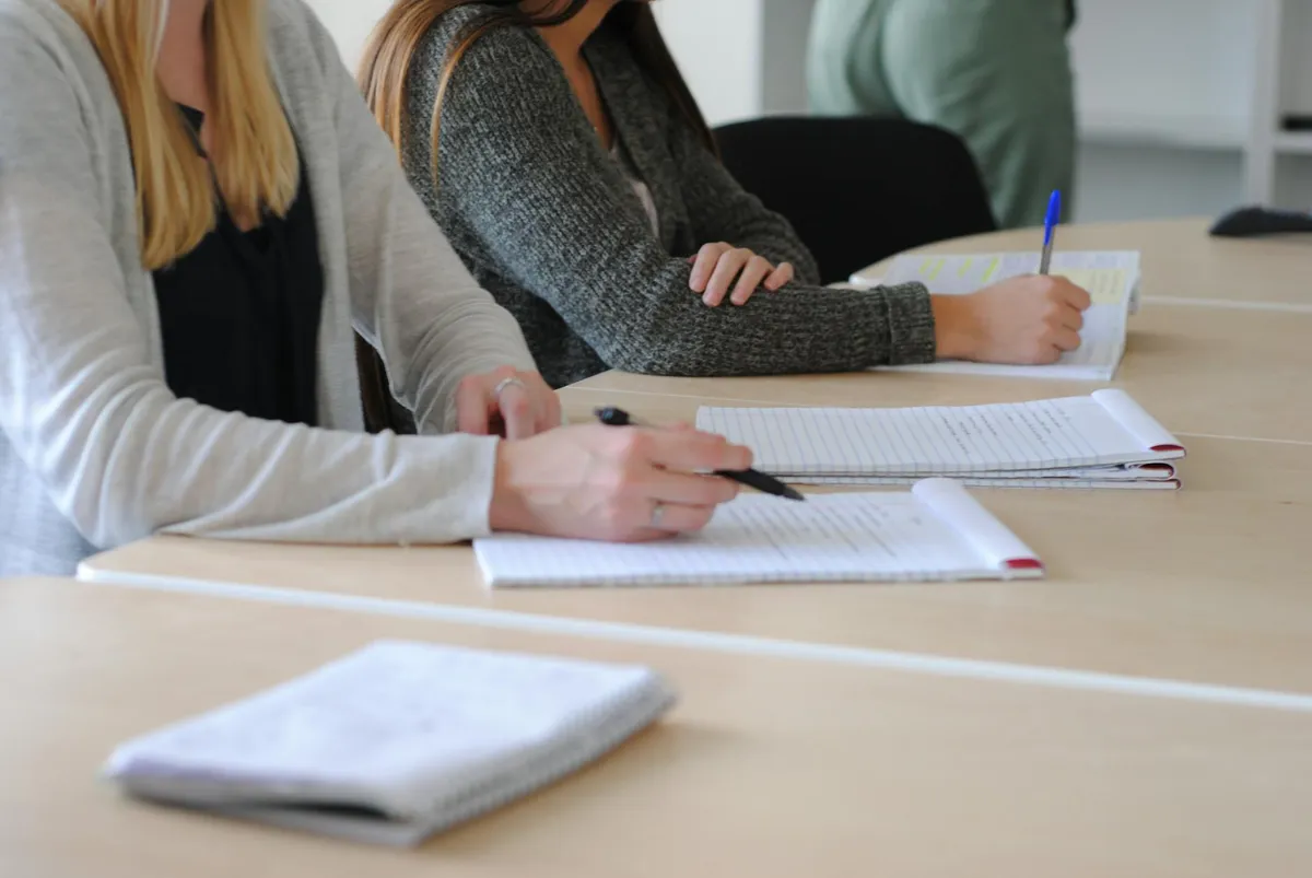Pessoa escrevendo texto acadêmico em laptop, folhas com anotações ao lado