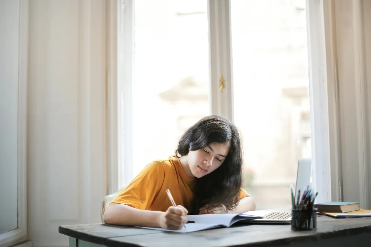 Estudante escrevendo redação em papel com caneta sobre mesa de estudos