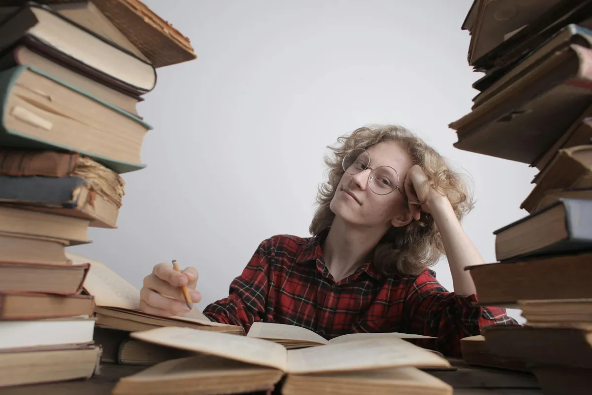 Pilha de livros acadêmicos abertos com marcações e anotações em mesa de estudo.