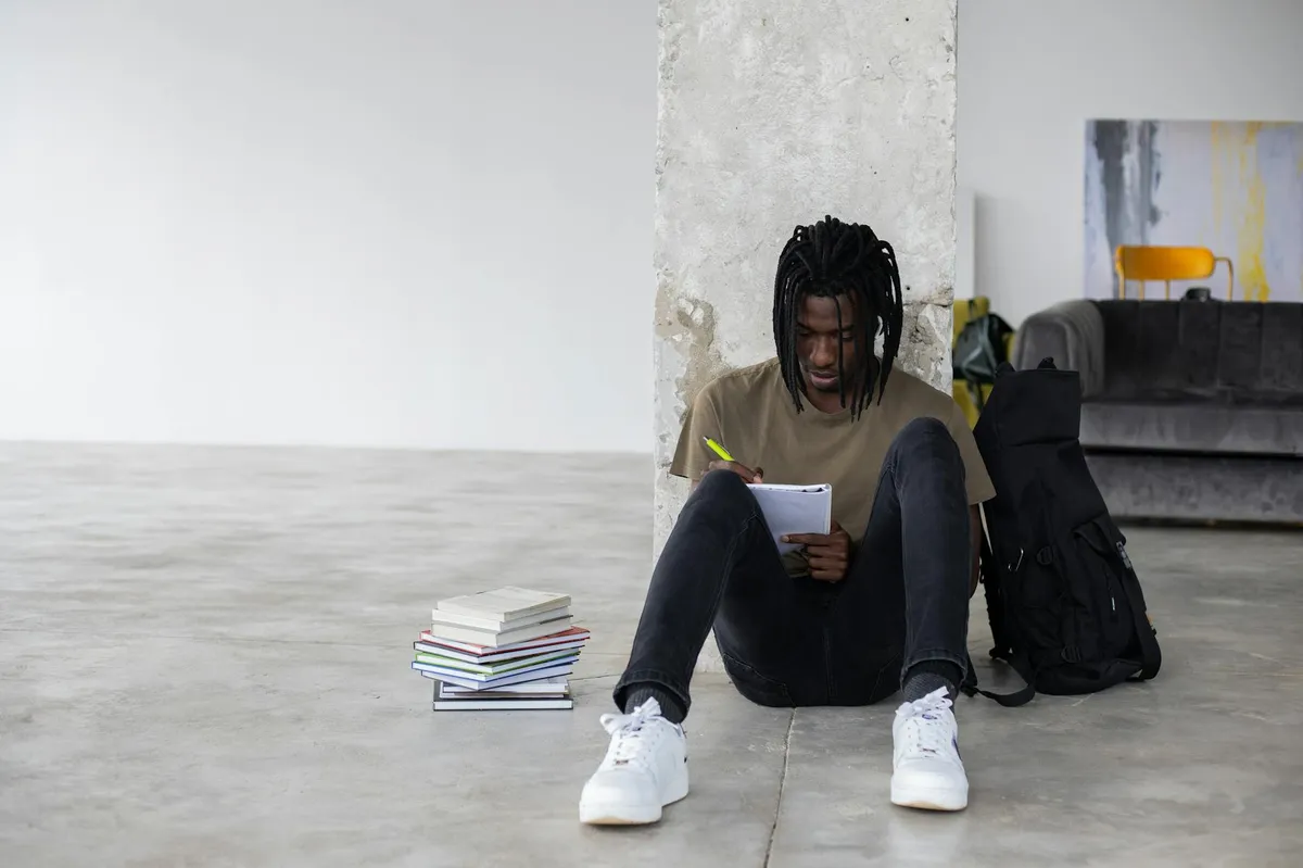 Estudante sentado com mochila nas costas olhando para o campus universitário, representando uma decisão difícil