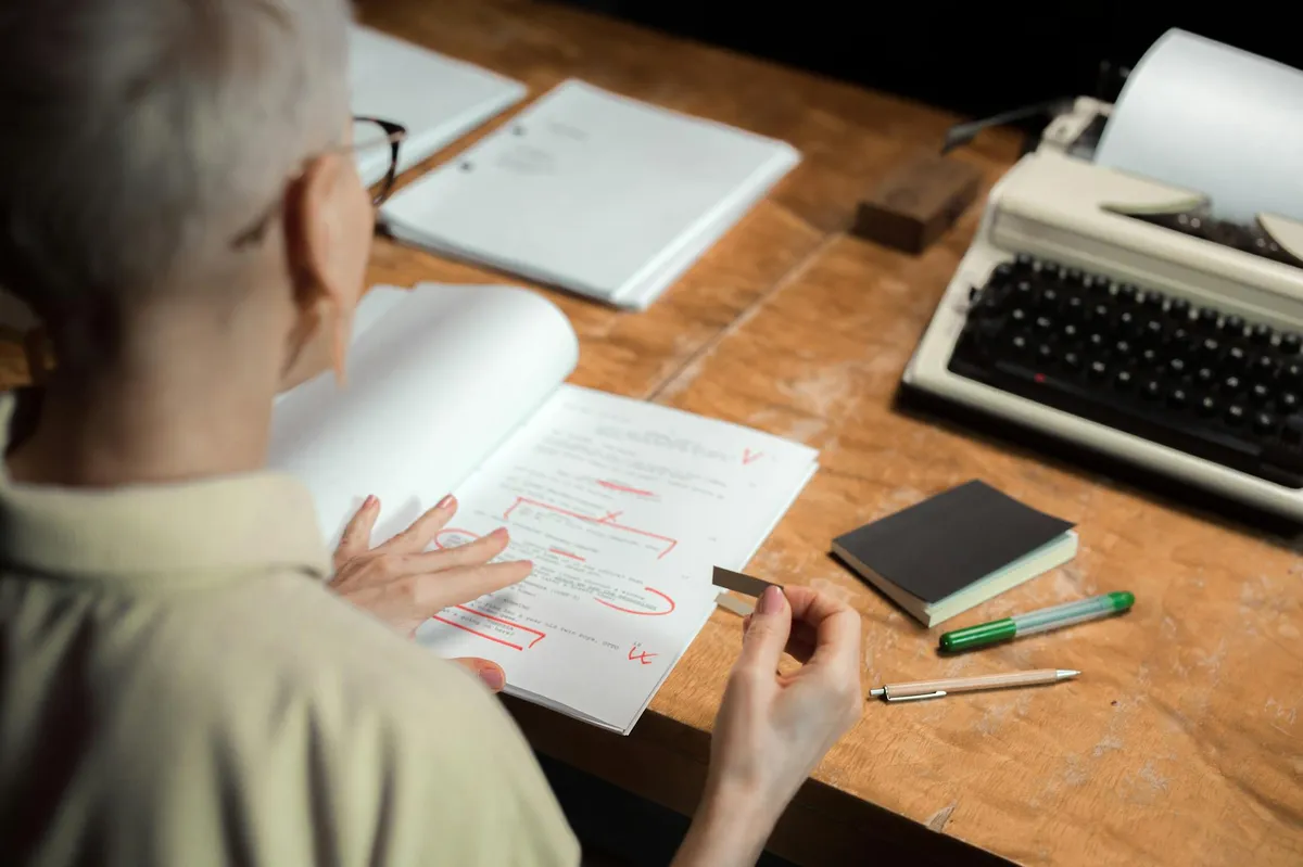 Pessoa revisando manuscrito com caneta vermelha sobre mesa de trabalho