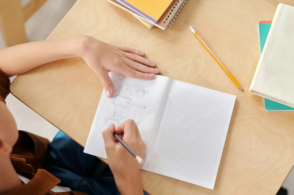 Pesquisadora escrevendo em caderno com caneta, mesa com livros abertos ao redor