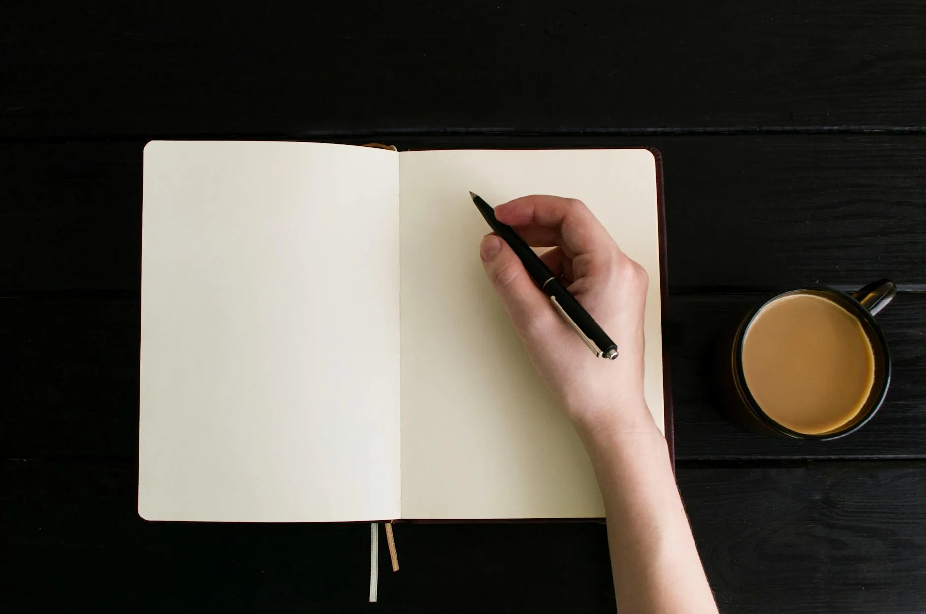 Caderno de rascunho com esboço de estrutura de capítulos ao lado de laptop e xícara de café