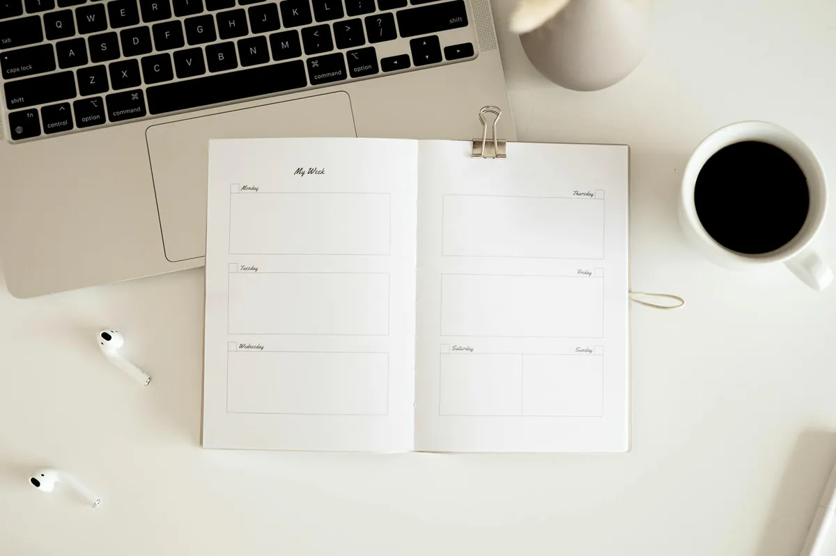 Caderno de planejamento semanal aberto sobre mesa com caneta e xícara de café