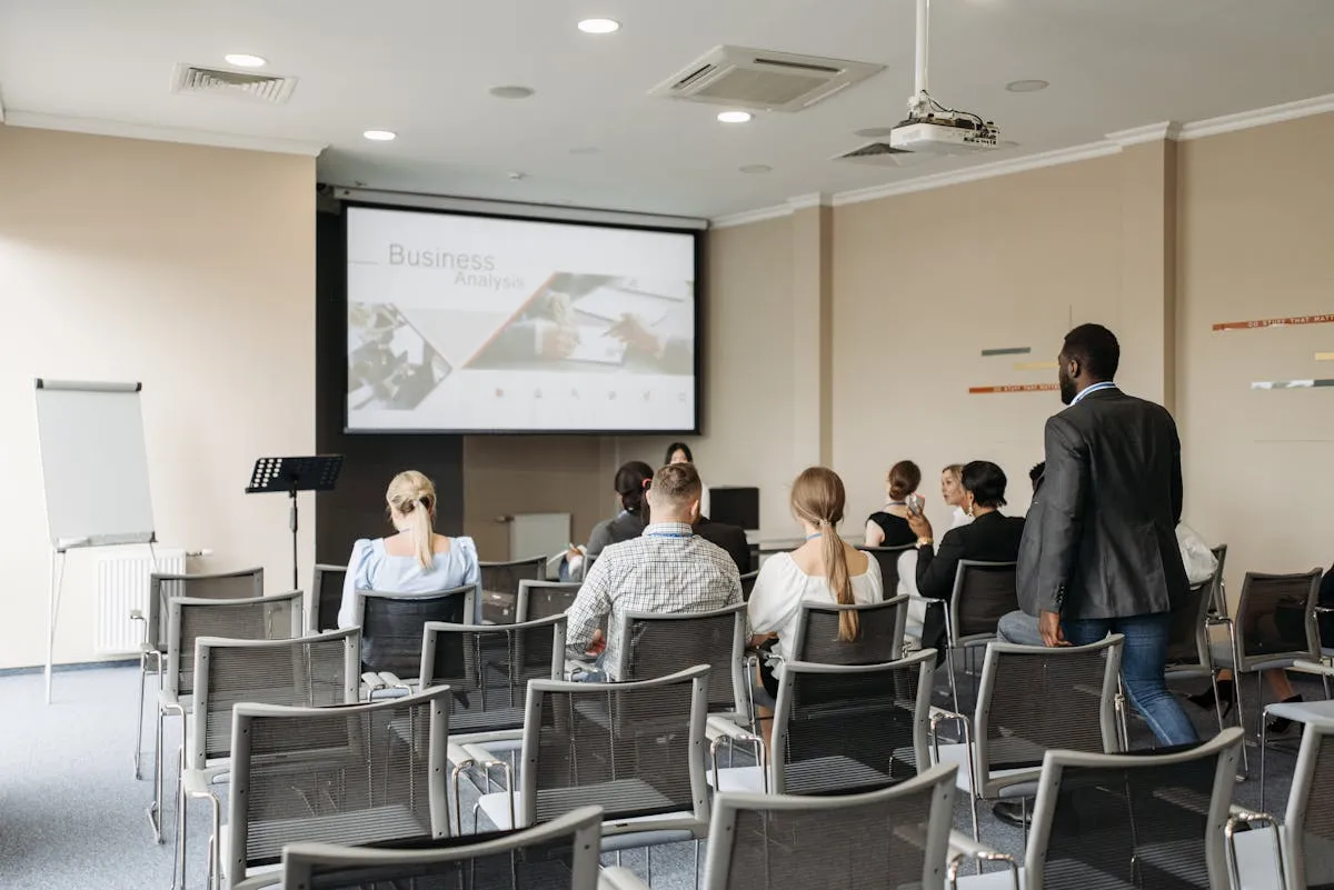 Pessoa de pé diante de tela de projeção em sala de apresentação, com cadeiras vazias ao fundo