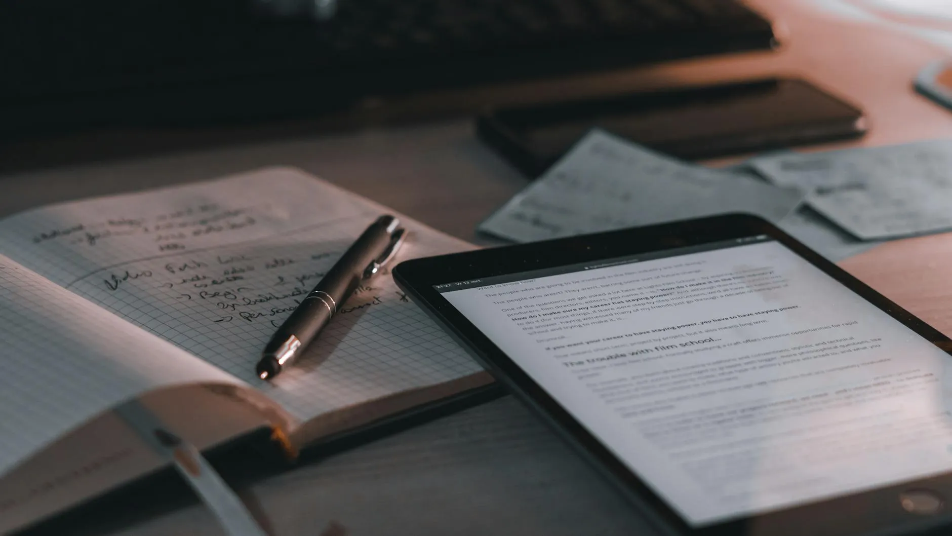 Caderno com anotações de pesquisa ao lado de tablet e computador em mesa de estudo