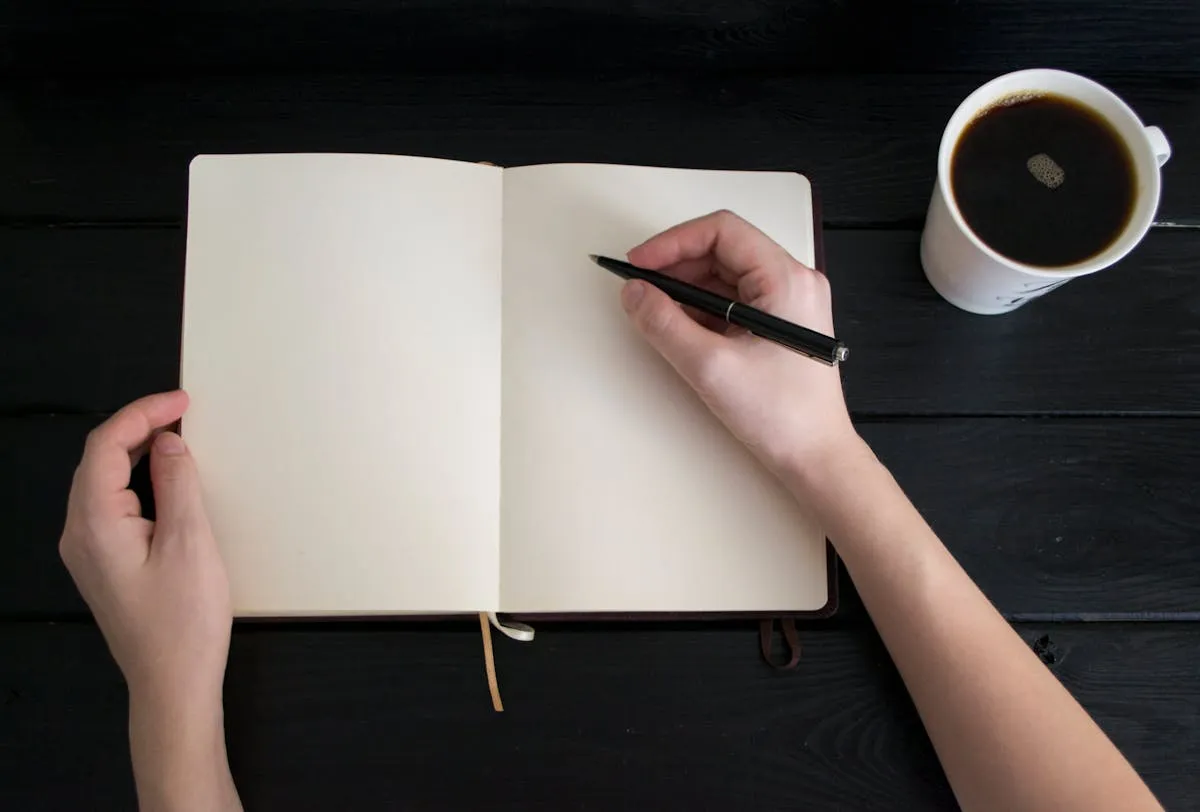 Pessoa abrindo caderno em mesa de trabalho com xícara de café