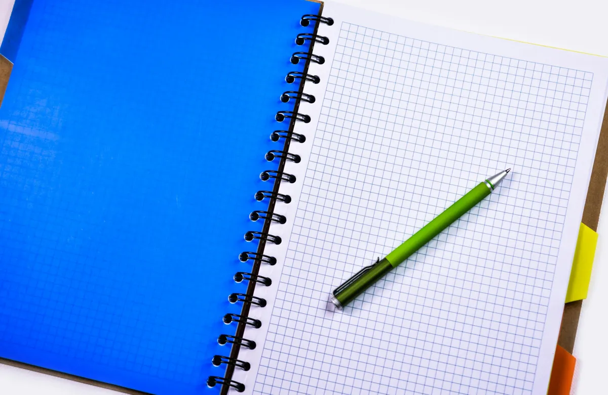 Pesquisadora escrevendo texto acadêmico com caderno de notas e computador