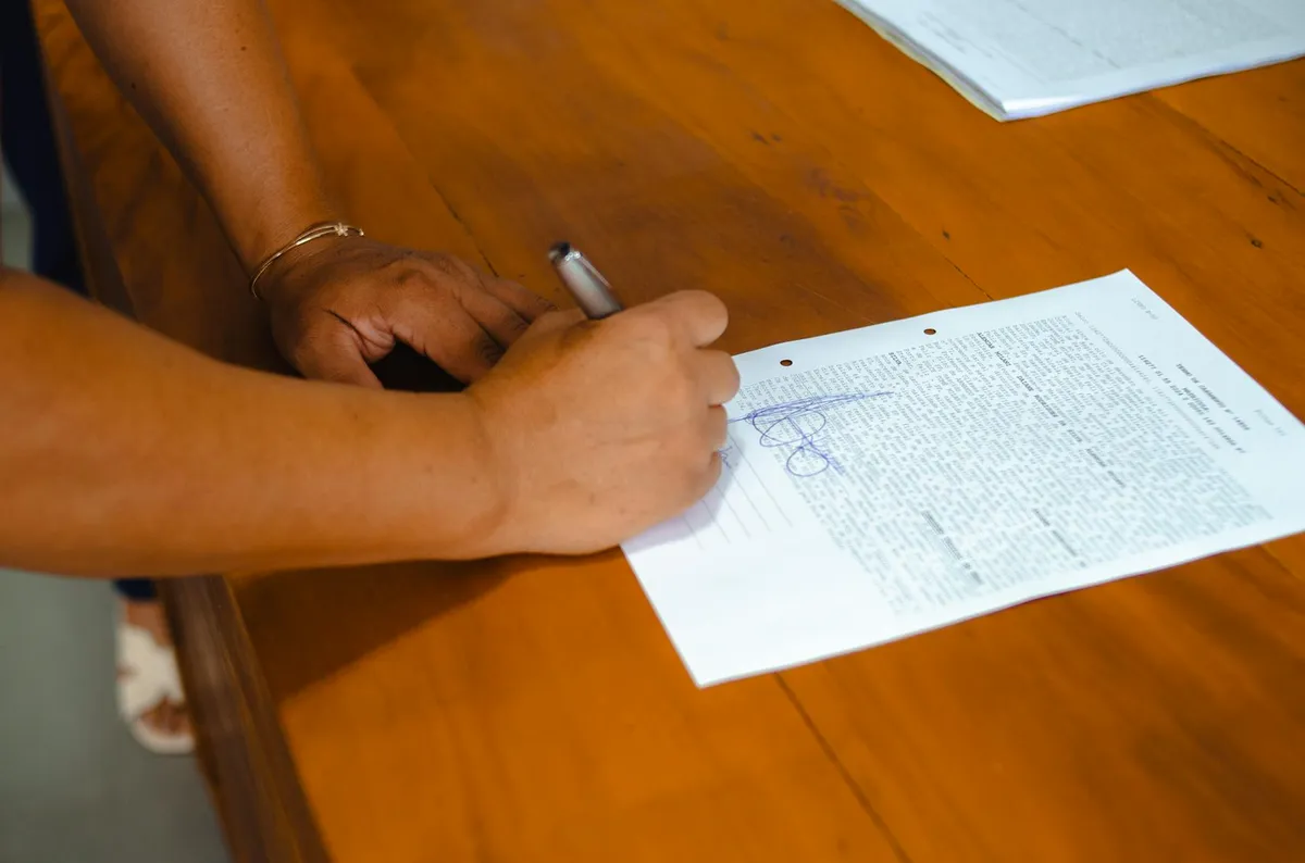 Pesquisadora lendo documento de consentimento informado em mesa de escritório com computador ao fundo