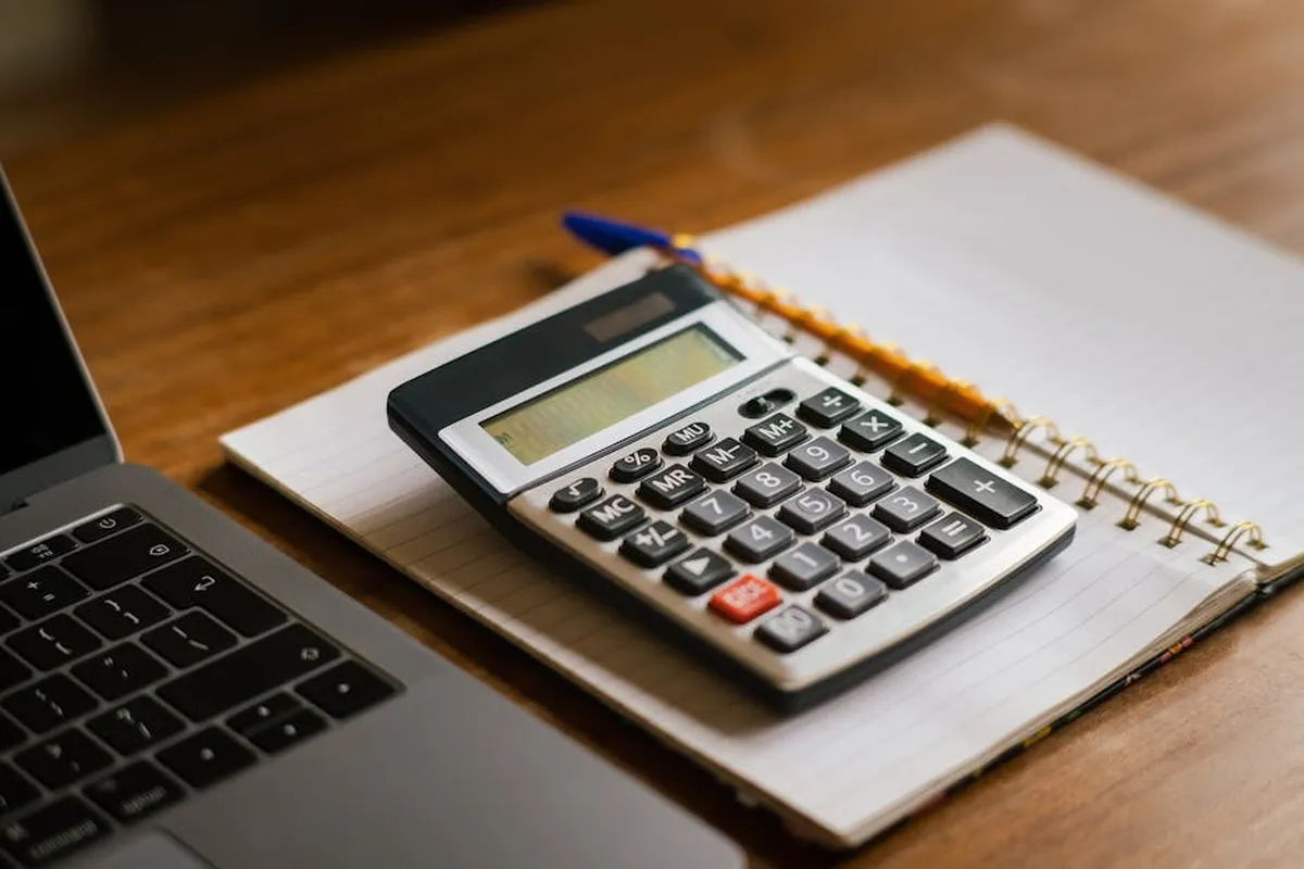 Notebook, calculadora e bloco de notas sobre mesa, representando planejamento financeiro na pós-graduação