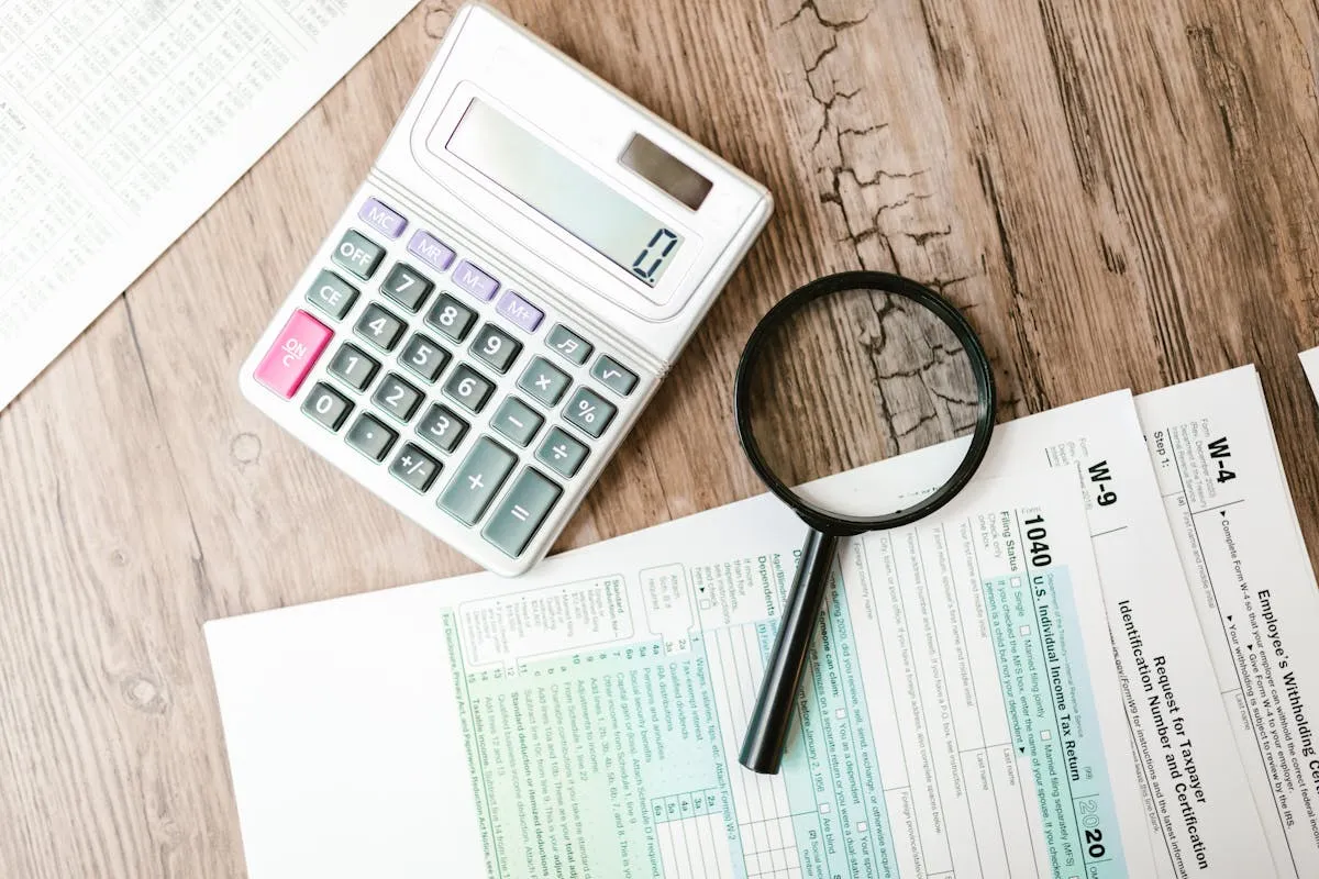 Pessoa preenchendo formulário fiscal com calculadora e documentos sobre mesa