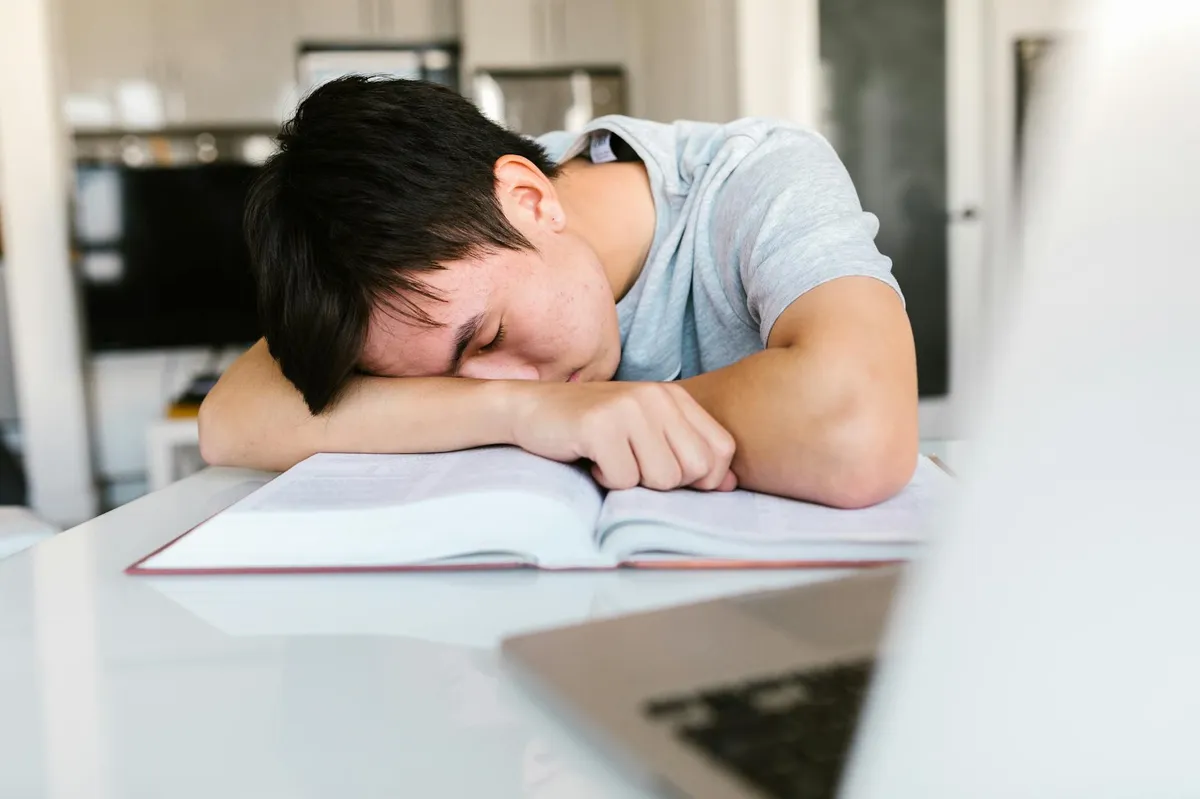 Estudante de doutorado em mesa de estudos com expressão de esgotamento