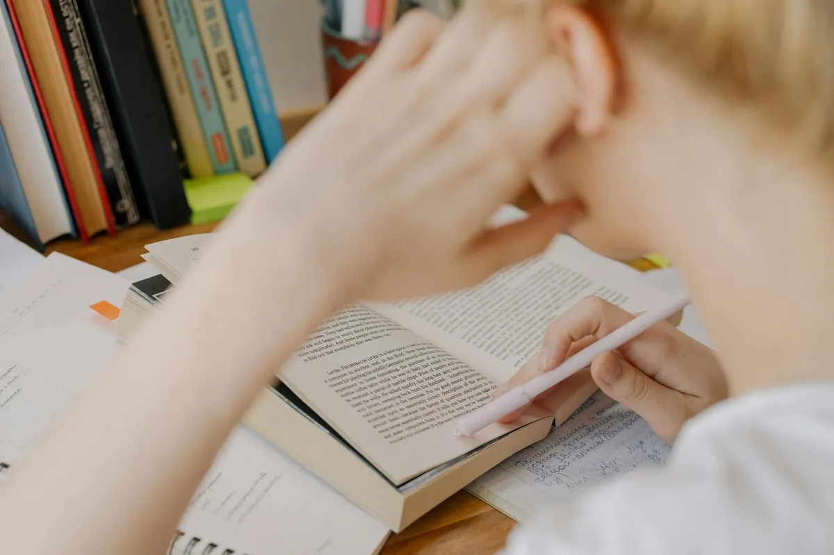 Professora lendo livros em biblioteca universitária, estudando para escrever dissertação em educação