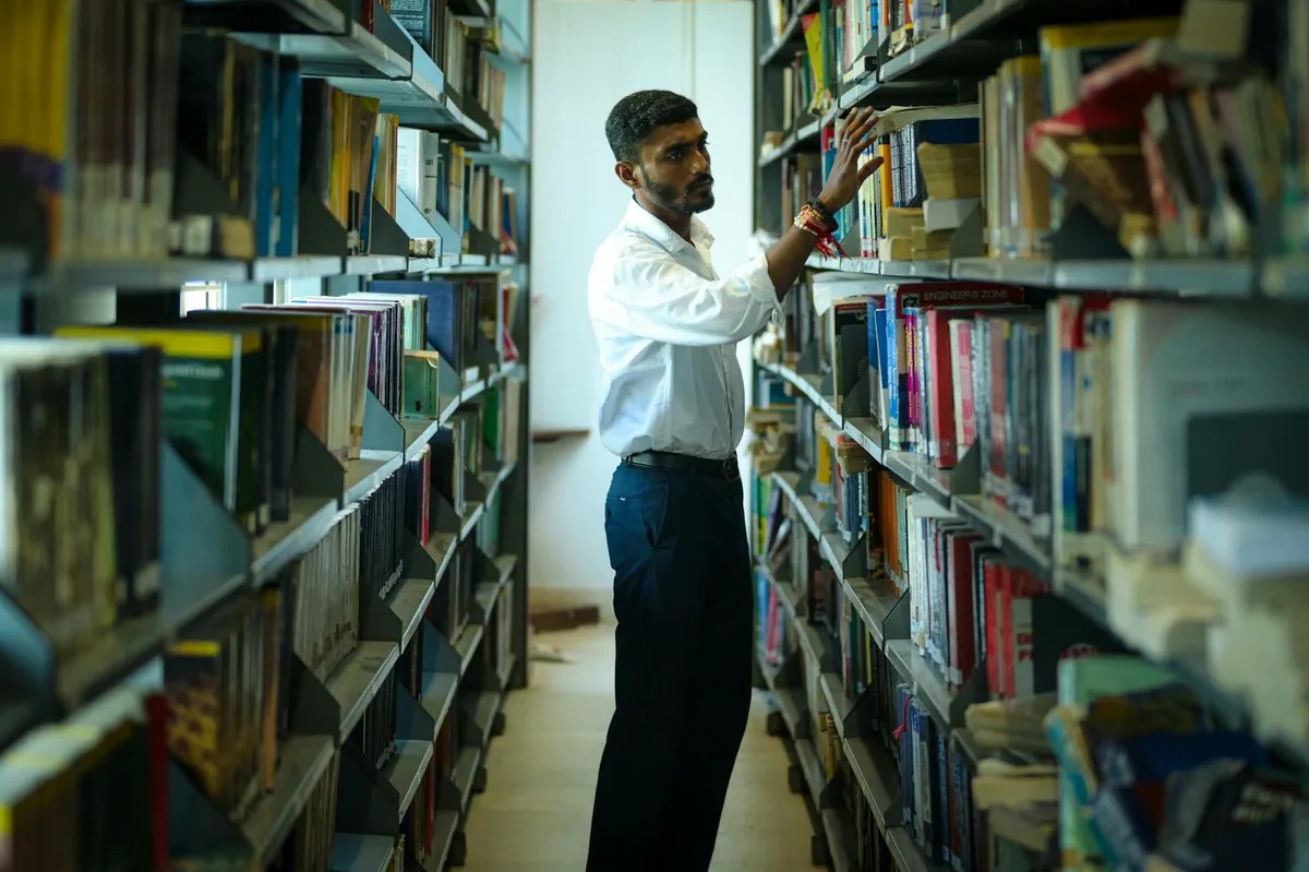 Pesquisador em biblioteca universitária com pilha de livros e anotações em mesa