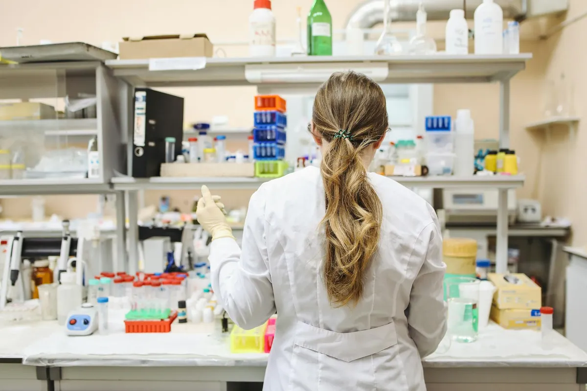 Laboratório farmacêutico com pesquisadora analisando amostras em equipamentos científicos