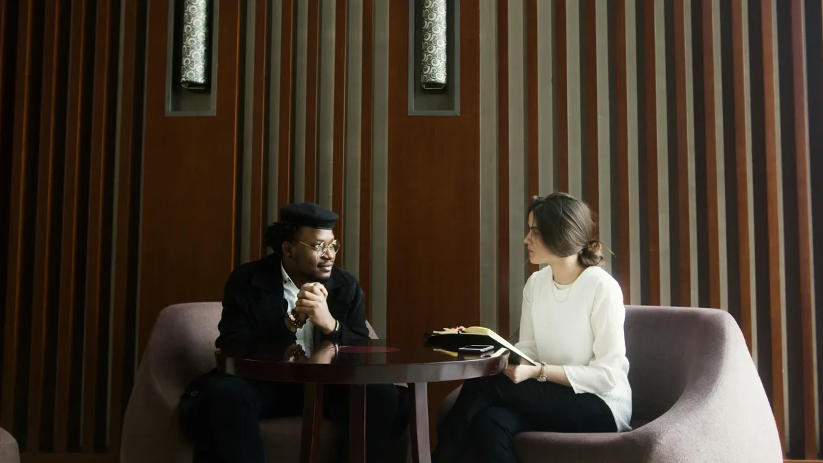 Duas pessoas sentadas em conversa com gravador sobre a mesa em ambiente de pesquisa