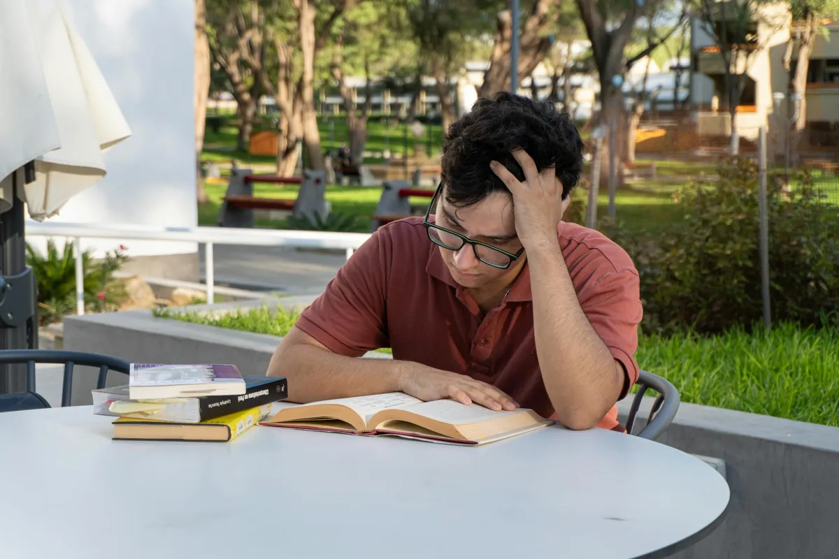 Pessoa estudando materiais acadêmicos em mesa com cadernos e computador