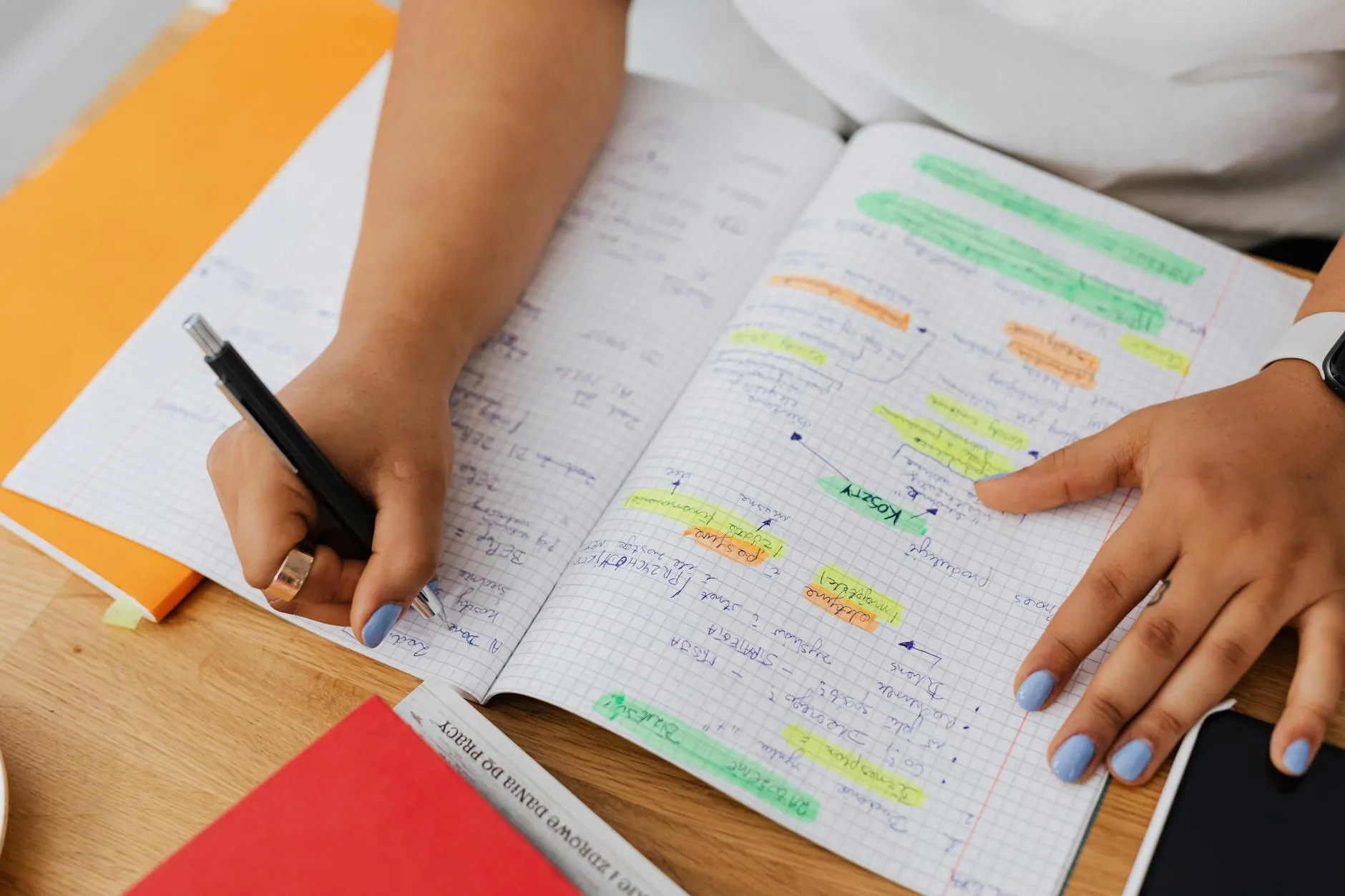Caderno de anotações aberto ao lado de livros acadêmicos sobre mesa