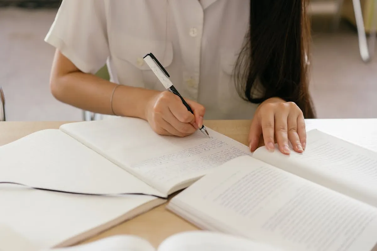 Pesquisadora fazendo anotações em caderno enquanto lê artigo científico