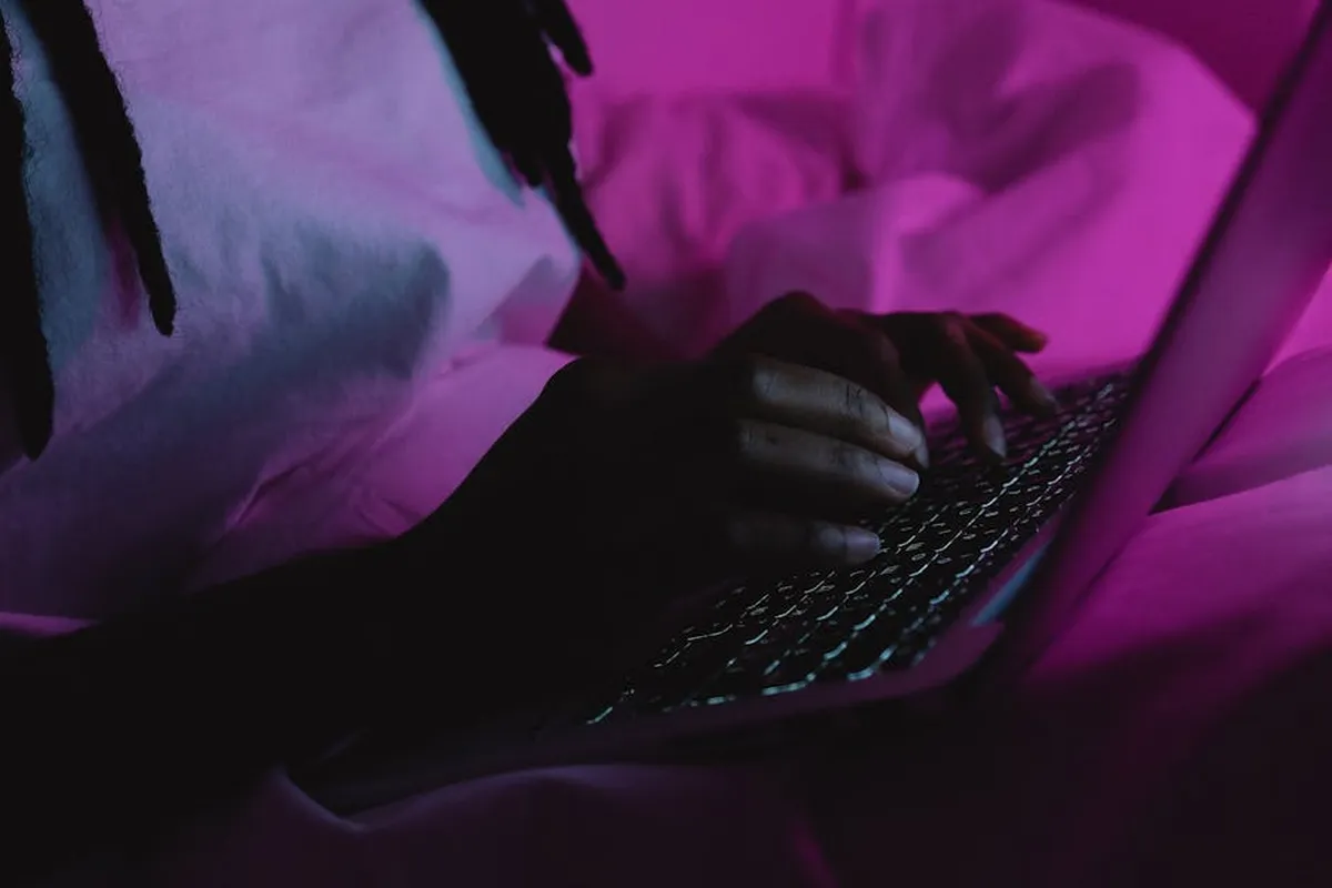 Pessoa escrevendo no computador com documentos acadêmicos na mesa, ambiente noturno