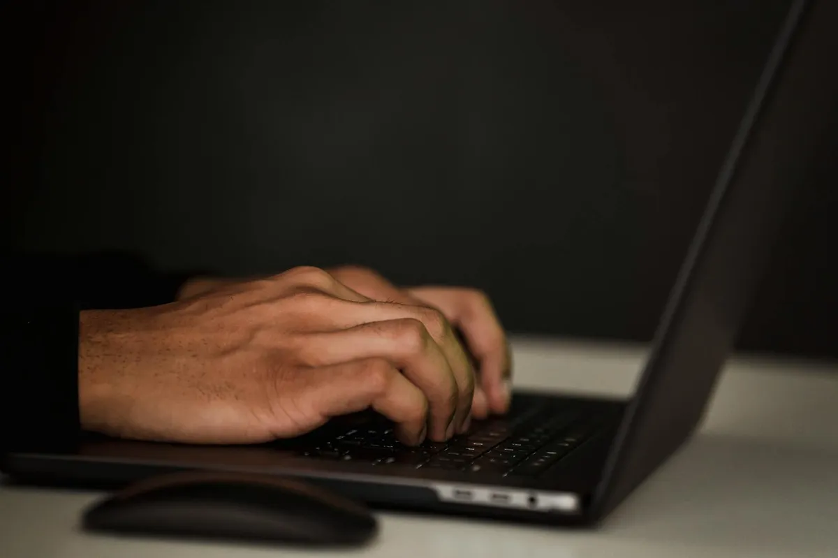 Silhueta de pessoa escrevendo em computador à noite, representando escrita anônima