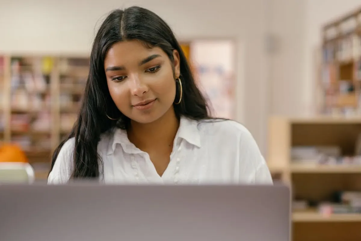 Estudante trabalhando com laptop em mesa de estudo com livros ao redor, representando pesquisa autônoma
