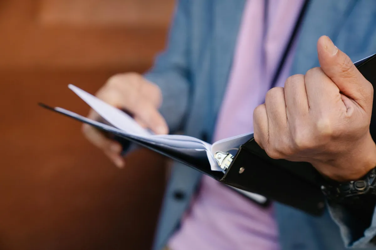 Estudante organizando documentos acadêmicos em mesa com computador e papéis
