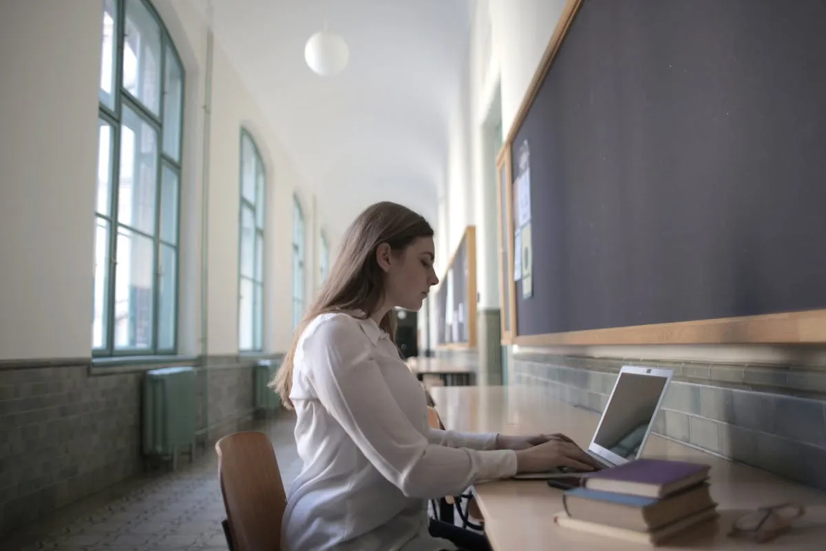 Mestranda usando computador com interface de IA aberta ao lado de livros acadêmicos