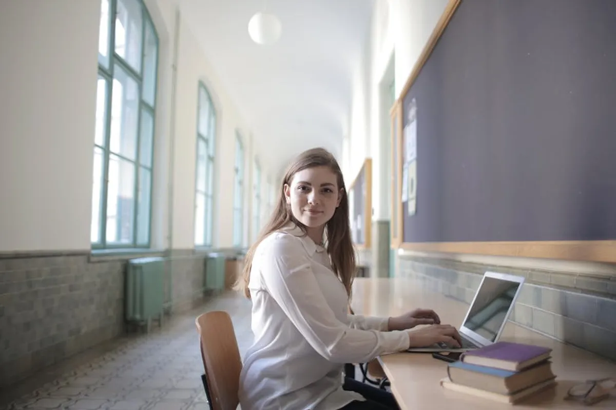 Estudante usando laptop para trabalho acadêmico, com cadernos e canetas sobre a mesa