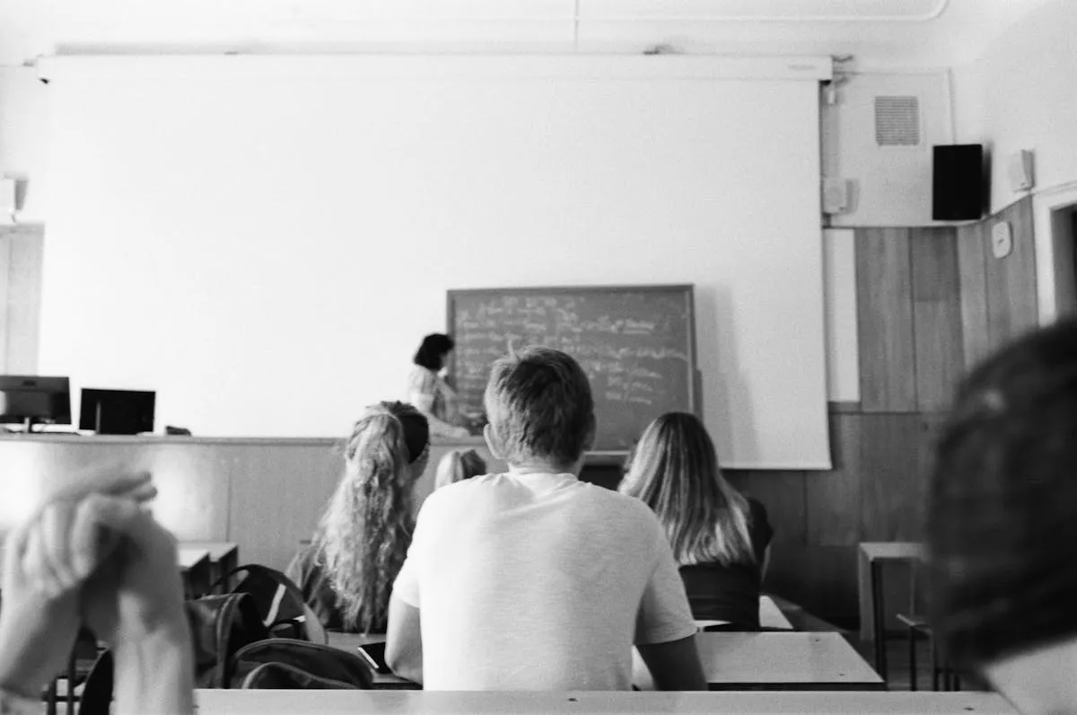 Professora em sala de aula universitária com livros e materiais educacionais
