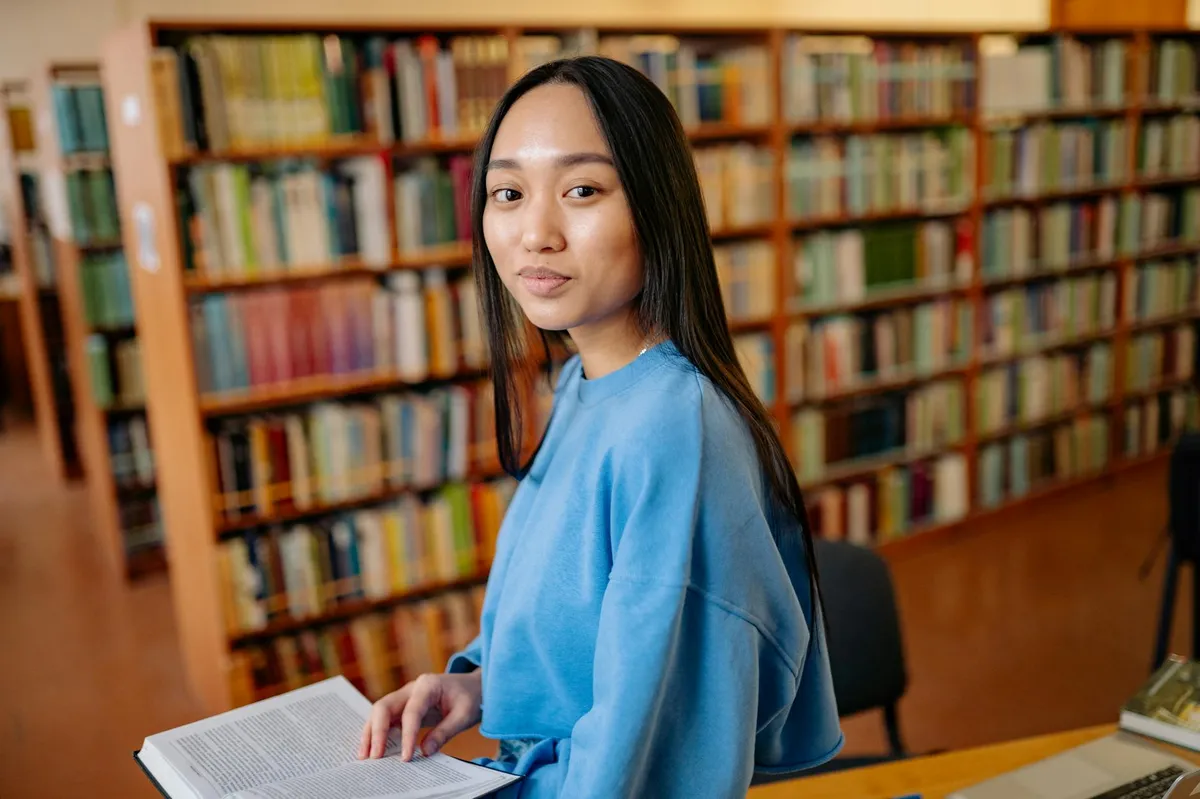 Estudante lendo livros acadêmicos em biblioteca universitária com muitos volumes