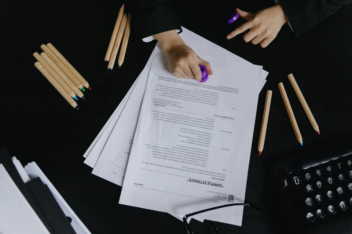 Estudante lendo documento acadêmico sobre mesa com laptop e livros