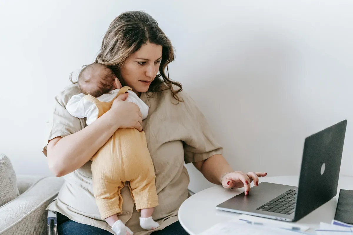 Mulher concentrada trabalhando em laptop com bebê recém-nascido no colo na mesa