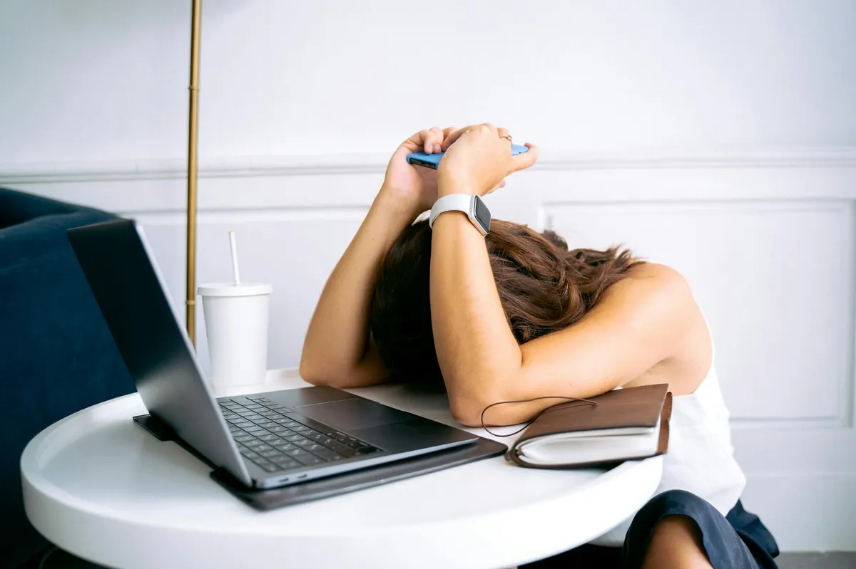 Jovem mulher demonstrando estresse com laptop e celular sobre a mesa, retratando exaustão digital